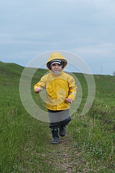 A blond boy in a yellow jacket runs in a green meadow