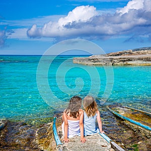 Blond and brunette kid girls sitting on beach port