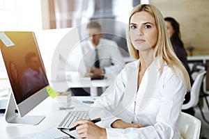 Blond business woman using computer at workplace in sunny office. Working for pleasure and success