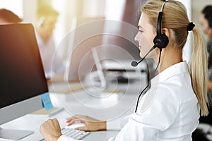 Blond business woman using headset for communication and consulting people at sunny office. Call center