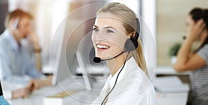 Blond business woman using headset for communication and consulting people at sunny office. Call center