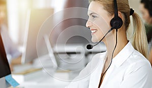 Blond business woman using headset for communication and consulting people at sunny office. Call center