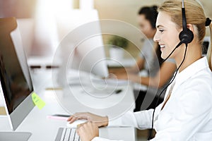 Blond business woman using headset for communication and consulting people at sunny office. Call center