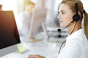 Blond business woman using headset for communication and consulting people at sunny office. Call center