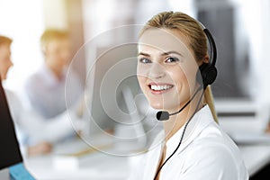 Blond business woman using headset for communication and consulting people at sunny office. Call center