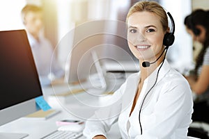Blond business woman using headset for communication and consulting people at sunny office. Call center