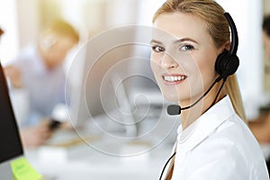 Blond business woman using headset for communication and consulting people at sunny office. Call center