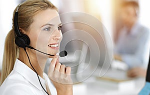 Blond business woman using headset for communication and consulting people at sunny office. Call center