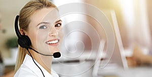 Blond business woman using headset for communication and consulting people at sunny office. Call center