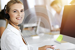 Blond business woman using headset for communication and consulting people at sunny office. Call center