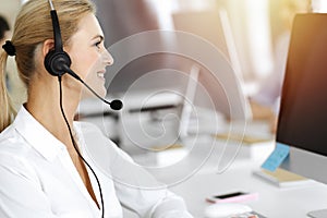 Blond business woman using headset for communication and consulting people at sunny office. Call center