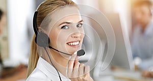 Blond business woman using headset for communication and consulting people at sunny office. Call center