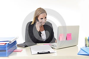 Blond businesswoman working at office laptop computer desk talking on mobile phone smiling