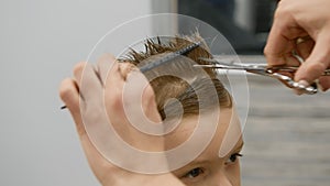 Blond caucasian boy is sitting in barber shop and hairdresser girl is cutting his hair. Child gets fashionable haircut