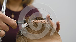 Blond caucasian boy is sitting in barber shop and hairdresser girl is cutting his hair. Child gets fashionable haircut