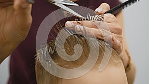 Blond caucasian boy is sitting in barber shop and hairdresser girl is cutting his hair. Child gets fashionable haircut