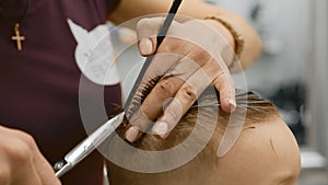 Blond caucasian boy is sitting in barber shop and hairdresser girl is cutting his hair. Child gets fashionable haircut