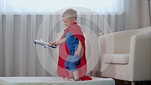 Blond caucasian boy super hero kid playing with toy air plane, jumping on mattress, trampoline with toy in his hands