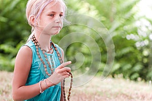 Blond caucasian girl practices meditation with rosaries outdoor summer day. yoga, mindfulness, harmony concept - girl making