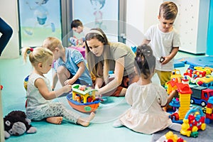 blond Caucasian teacher helping kids to build things properly in the nursery, a playground full of toys, creative