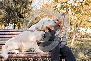 Blond caucasian woman sitting with her golden labrador retriever dog on the bench in the park