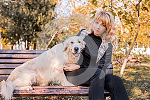 Blond caucasian woman sitting with her golden labrador retriever dog on the bench in the park