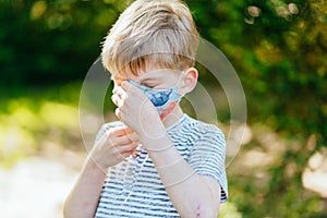 Blond child boy puts a face protective mask outdoors. Health care concept. Protective medical mask against infectious