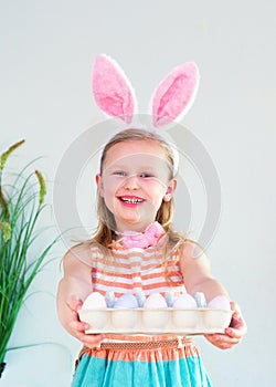 Blond child girl wearing bunny ears on Easter day play with Easter eggs at home