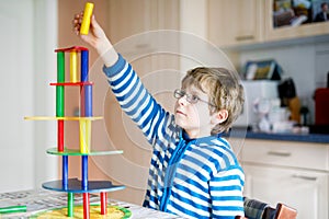 Blond child with glasses playing with lots of colorful wooden blocks game indoor. Active funny kid boy having fun with