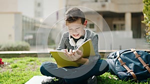 Blond child reading book sitting on grass at park