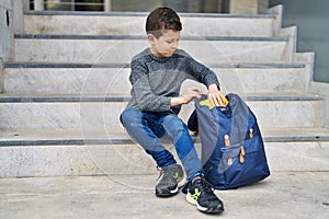 Blond child student holding book sitting on stairs at school