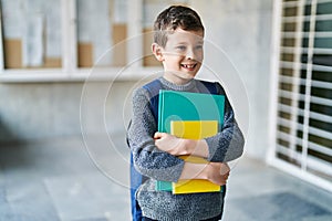 Blond child student holding books standing at school
