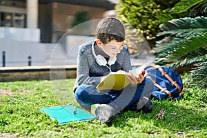 Blond child student reading book sitting on grass at park