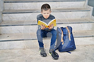 Blond child student reading book sitting on stairs at school