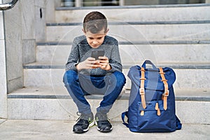 Blond child student using smartphone sitting on stairs at school