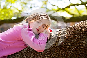 Blond children kid girl having a nap lying on a tree photo