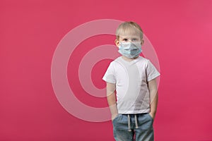A blond European-looking child boy stands in a medical mask from a coronavirus and looks at the camera