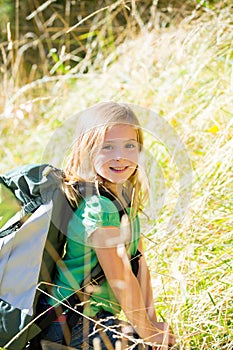 Blond explorer kid girl walking with backpack in grass