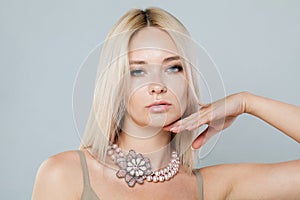 Blond fashion model woman with clear fresh perfect skin and long blonde hair wearing jewelry pearl necklace posing on gray studio
