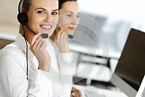 Blond female customer service representative and her colleague are consulting clients online using headset. Call center