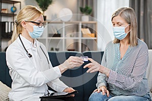 Blond female doctor in medical coat, glasses and protective mask, measuring oxygen saturation and heart rate with a