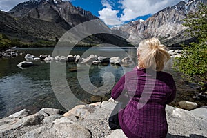 Blond female sits alone by Convict Lake in the springtime, located off of US-395, near Mammoth Lakes California in the eastern