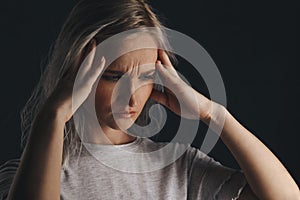 Blond female in stress with headache holding her hands on the head. Migraine concept.