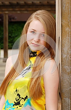 Blond female teen leaning on a wood pillar