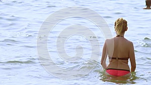 Blond girl in a bathing suit and black sunglasses. woman in a red swimsuit walks into the sea