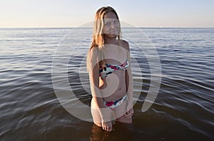 Blond girl in a bikini standing in the sea water. Beautiful young woman in a colorful bikini on sea background