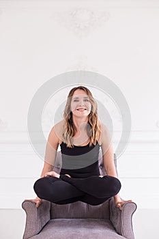 Blond girl in black sportsuit sits on gray chair in lotus pose