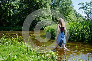 Blond girl blue mottled dress wade flowing river