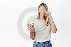 Blond girl cry and watch something sad on smartphone app, crying woman wiping tears and sobbing with mobile phone, white
