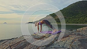 Blond girl does yoga poses on rocky ocean beach